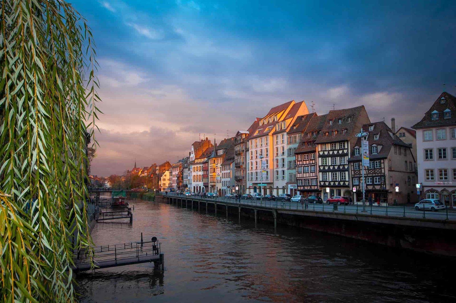 A photo of a river in Strasbourg, France. There are buildings along the river, and the sky is orange and blue