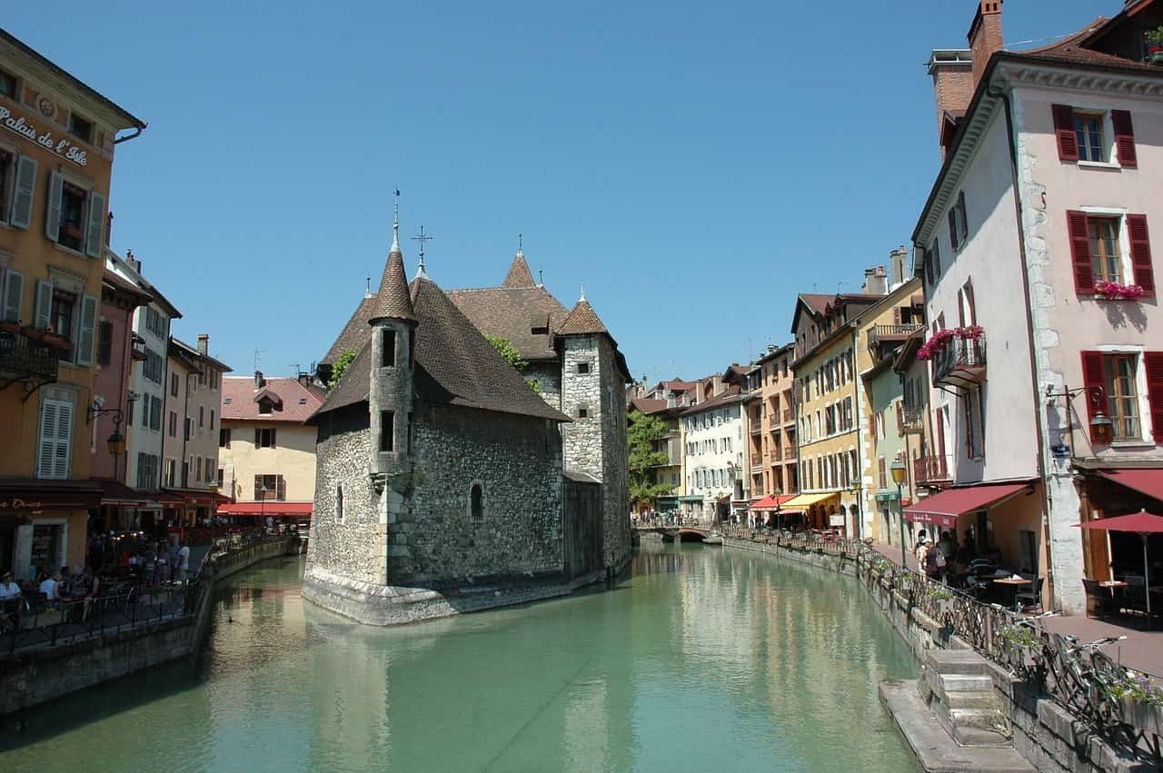 A picturesque view of the Palais de l'Isle, a medieval castle turned prison, surrounded by colorful buildings and a canal in Annecy, France