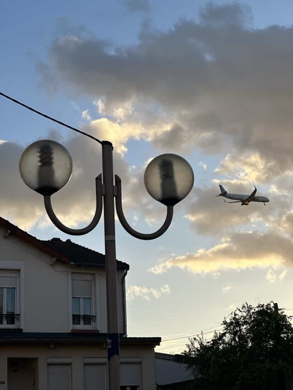 A photo of a plane flying low over a residential area at dusk, with streetlights illuminating the sky