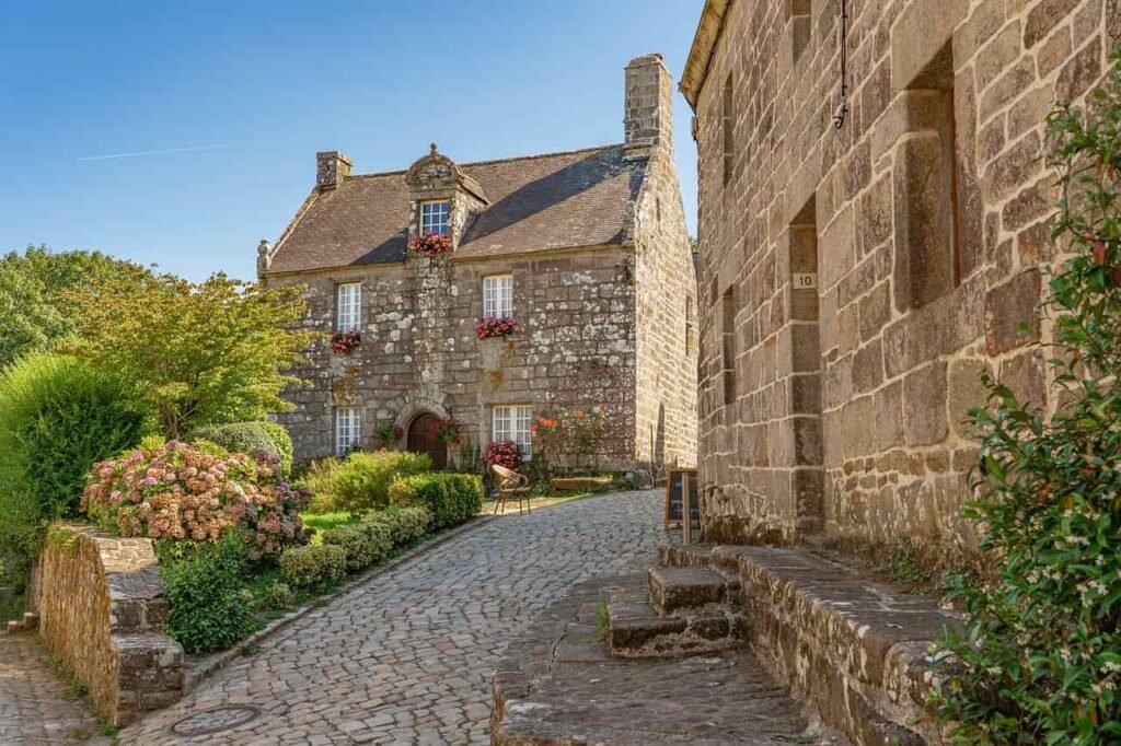 A picturesque stone cottage with a flower-filled garden in a narrow cobblestone street in Normandy, France