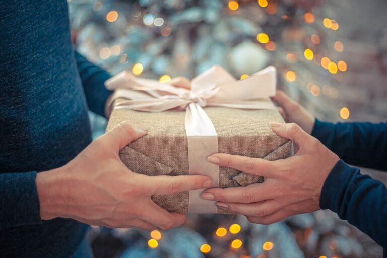 Two hands exchanging a wrapped gift with a warm, festive background